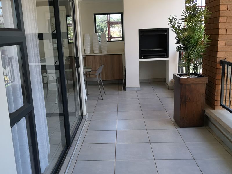 Covered balcony featuring tiled flooring, a built-in braai, and large sliding glass doors providing seamless access to the interior living space.