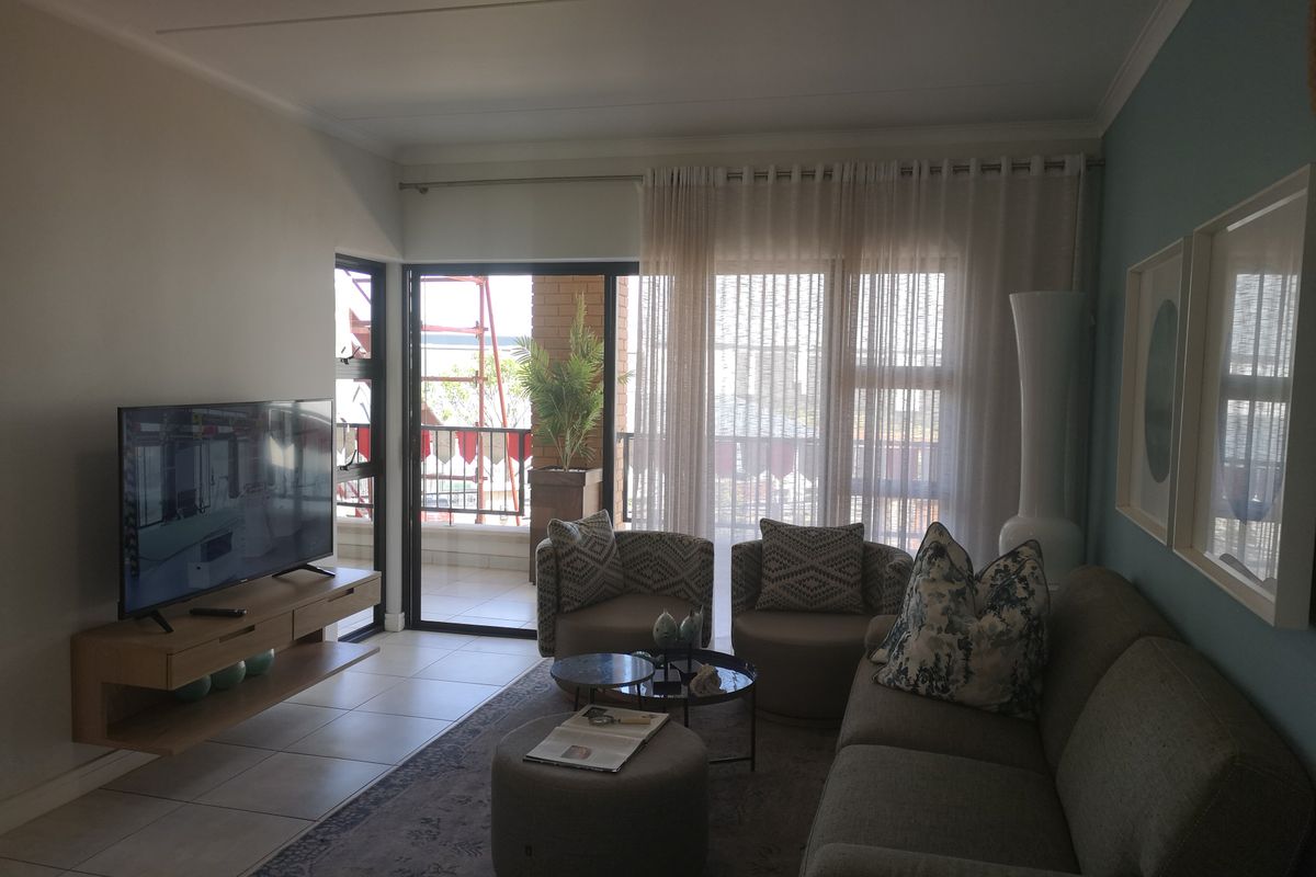 A comfortable living room featuring tiled flooring, a floating media console, and large sliding glass doors that provide access to an outdoor balcony area.