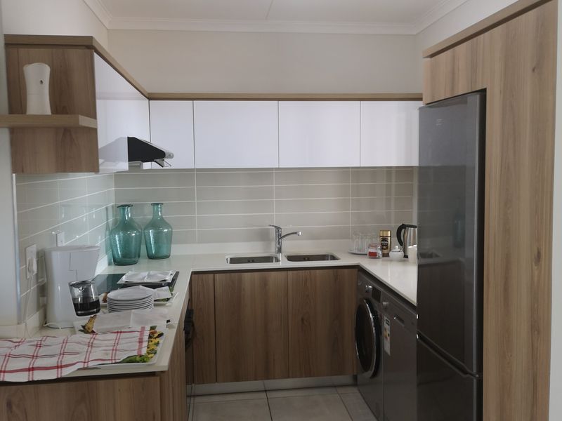 Modern galley-style kitchen featuring wood-grain and white cabinetry, tiled backsplash, integrated appliances, and durable floor tiles.