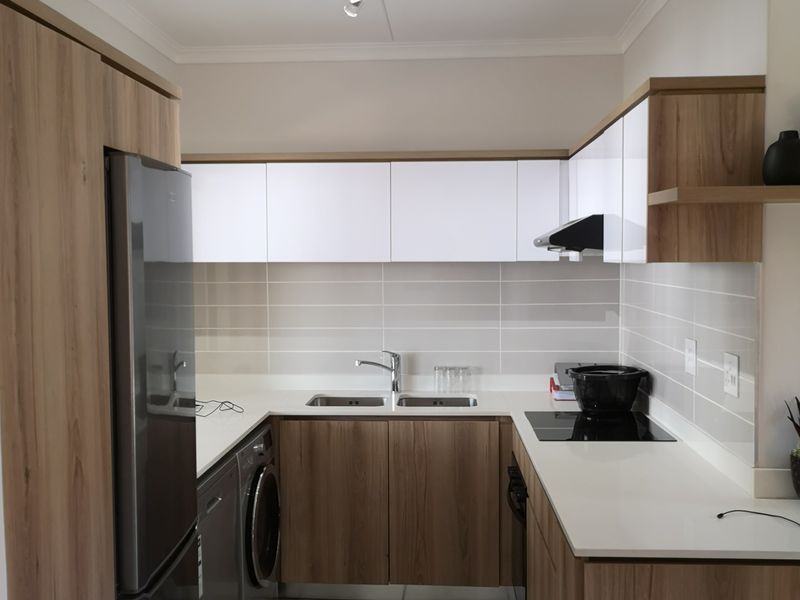 Modern kitchen featuring wood-grain and white cabinetry, stone-look countertops, integrated appliances, and a tiled backsplash with a functional double sink layout.