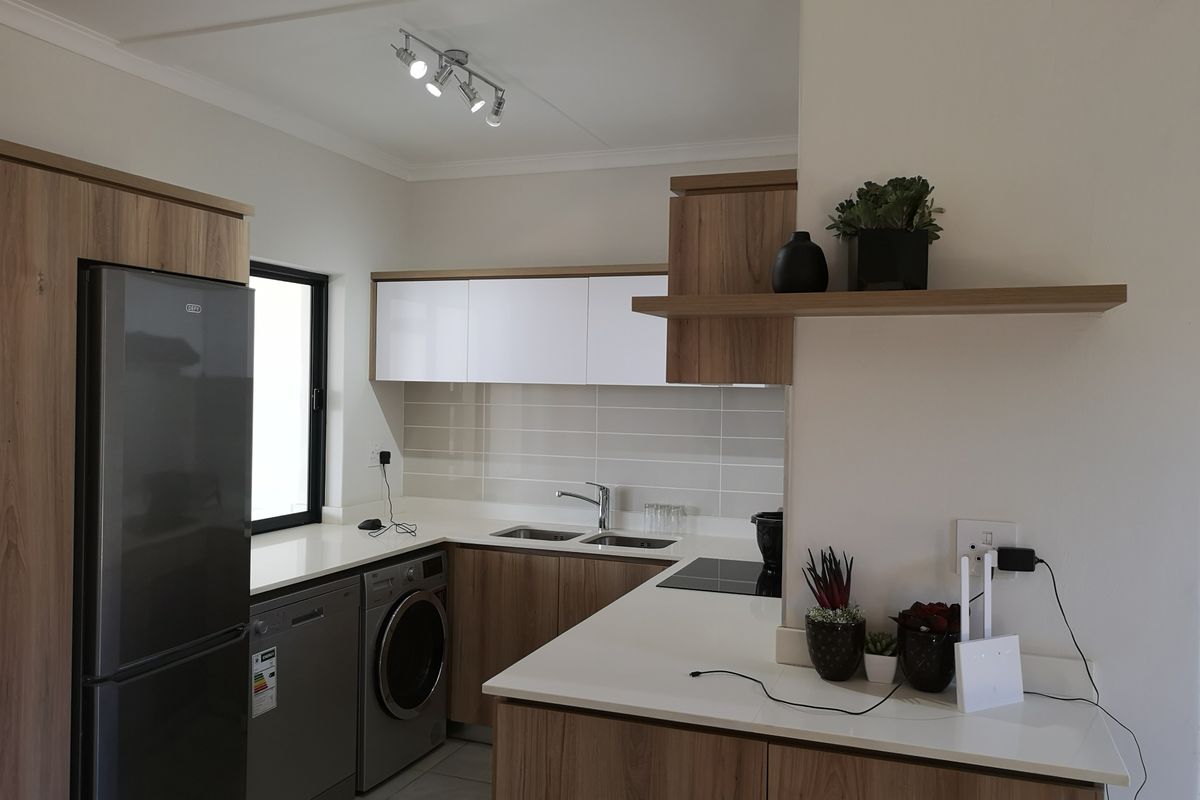 Modern kitchen featuring wood-grain cabinetry, white stone countertops, tiled backsplash, and integrated appliances, offering a clean and functional cooking space.