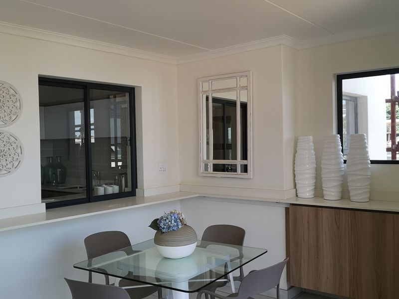 An open-plan dining area featuring tiled flooring, built-in cabinetry, and a pass-through window connecting to the kitchen space.
