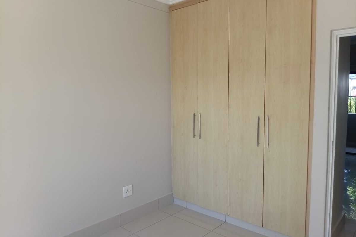 A clean, empty bedroom featuring light-toned built-in cupboards and neutral tiled flooring, offering a versatile space ready for personalization.