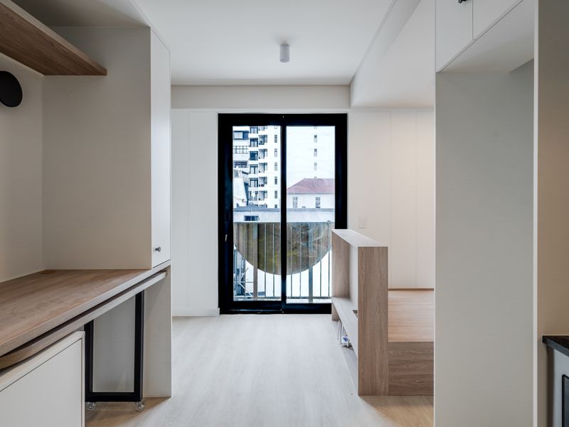 Modern open-plan apartment interior featuring light wood finishes, built-in cabinetry, and a sliding glass door leading to a balcony.
