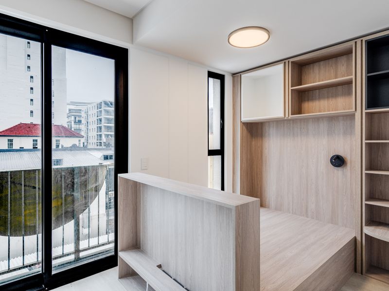 Modern bedroom featuring custom built-in light wood cabinetry and shelving with large sliding glass doors providing natural light and urban views.