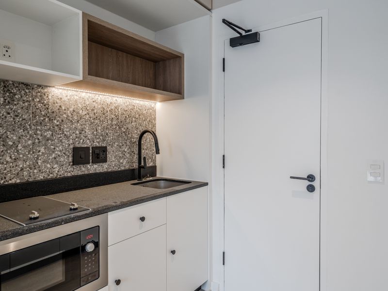 A modern, compact kitchen featuring a terrazzo backsplash, stone countertop, built-in cooktop, microwave, and sleek cabinetry with integrated lighting.