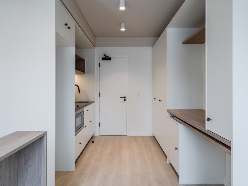 Modern, minimalist kitchen featuring clean white cabinetry, integrated appliances, wood-tone accents, and recessed lighting in a bright, functional layout.