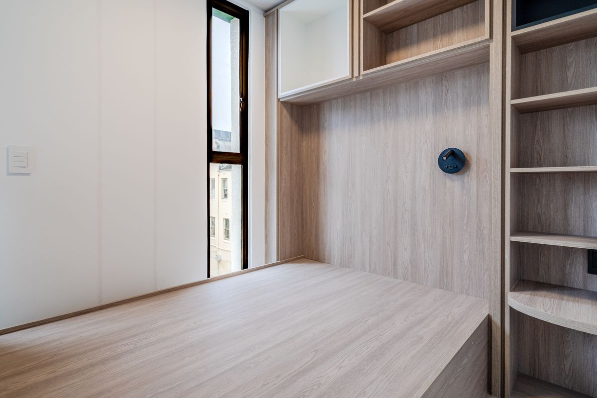 A modern bedroom featuring custom built-in light wood cabinetry, integrated shelving, and a built-in bed frame with a vertical window.
