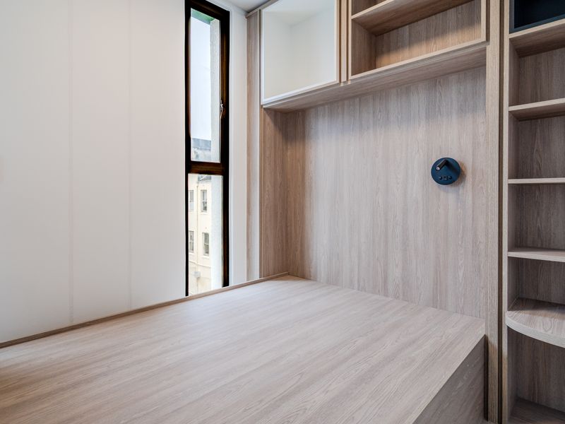 A modern bedroom featuring custom built-in light wood cabinetry, integrated shelving, and a built-in bed frame with a vertical window.