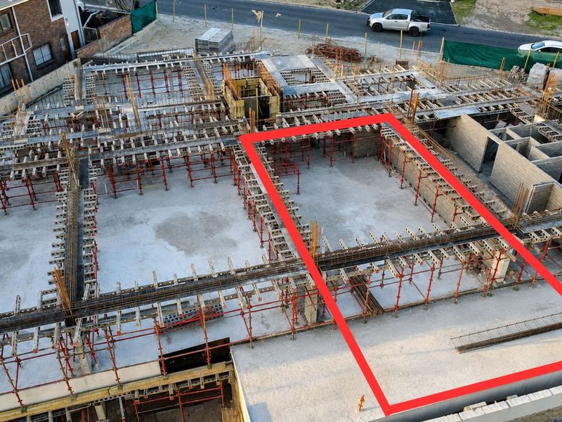 Aerial view of a residential apartment construction site showing the concrete foundation and steel reinforcement framework in progress.