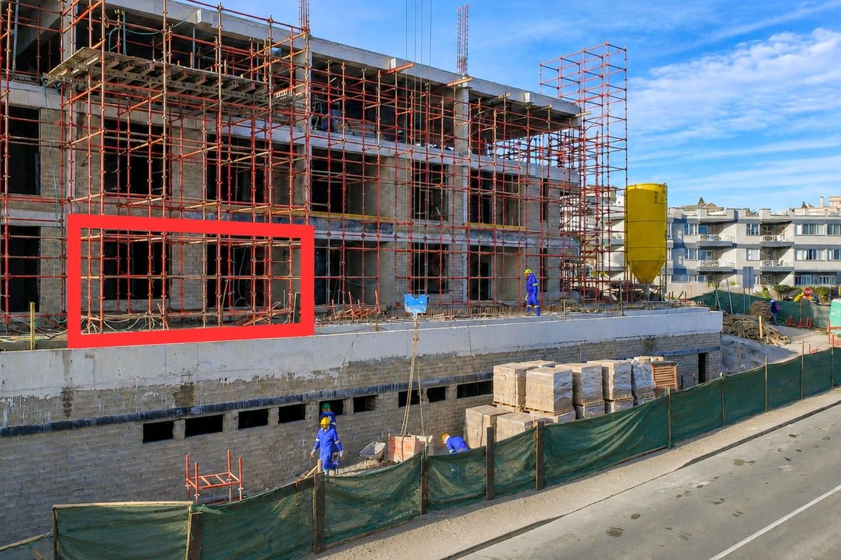 An aerial view of an apartment building under construction, featuring exposed concrete framework and extensive scaffolding on the exterior facade.