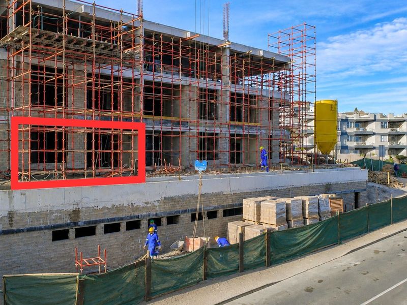 An aerial view of an apartment building under construction, featuring exposed concrete framework and extensive scaffolding on the exterior facade.