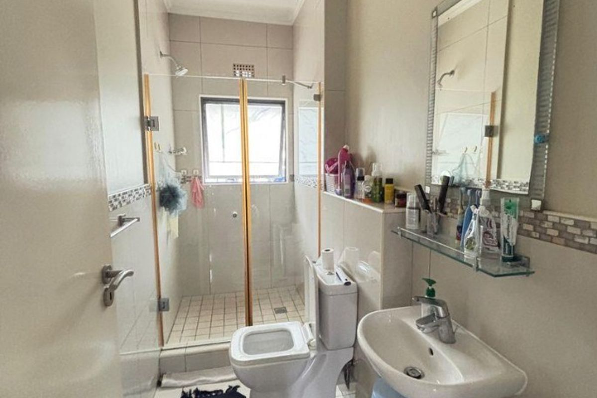 A functional bathroom featuring a glass-enclosed shower, pedestal basin, toilet, and tiled finishes throughout.