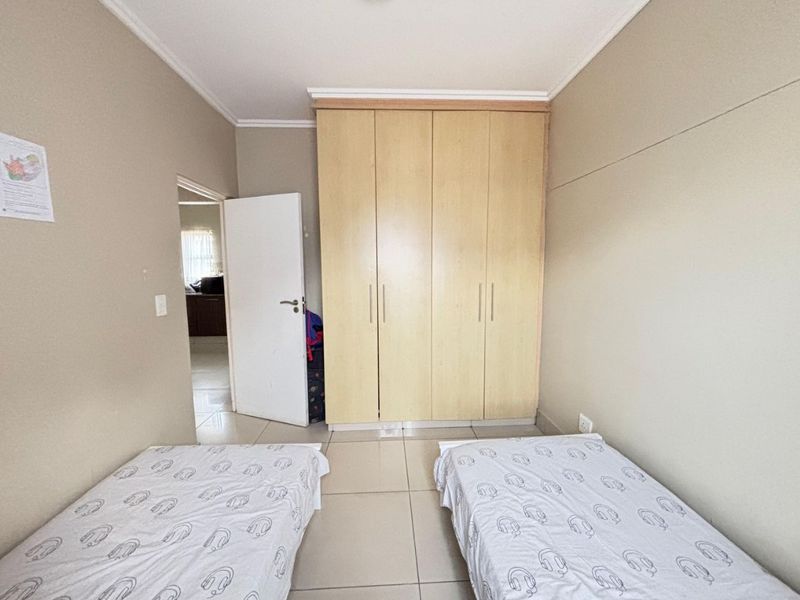 A functional bedroom featuring neutral wall tones, tiled flooring, and a large built-in wooden wardrobe providing ample storage space.