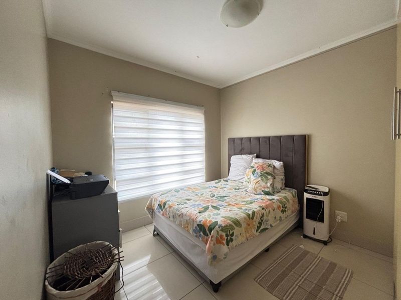 A functional bedroom featuring neutral wall tones, tiled flooring, and a window fitted with modern roller blinds.