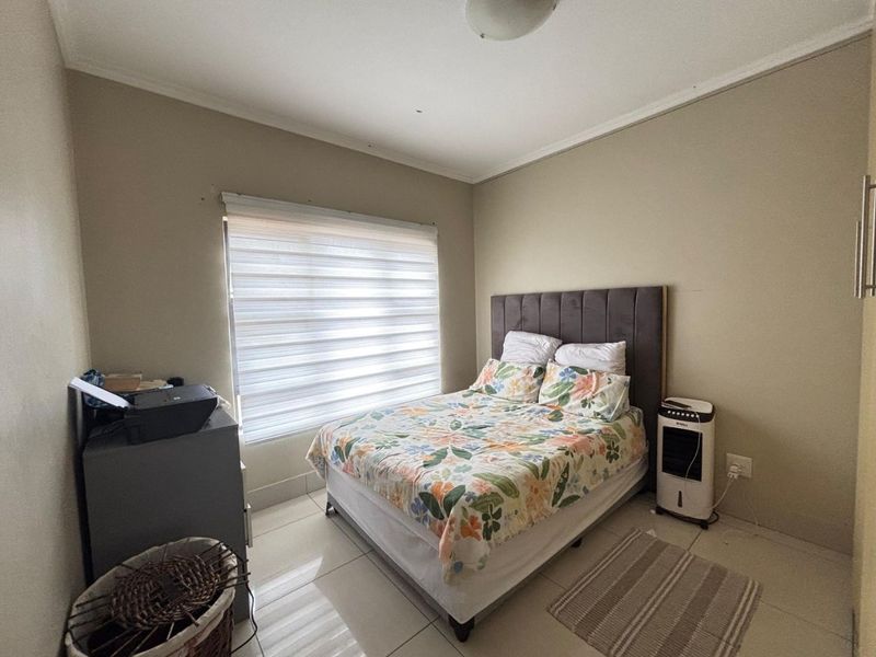 A functional bedroom featuring tiled flooring, neutral wall finishes, and a window fitted with modern roller blinds.