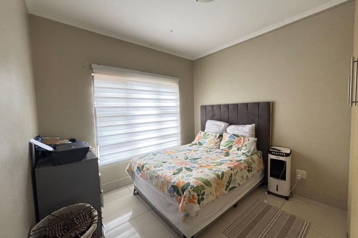 A functional bedroom featuring tiled flooring, neutral wall finishes, and a window fitted with modern roller blinds.