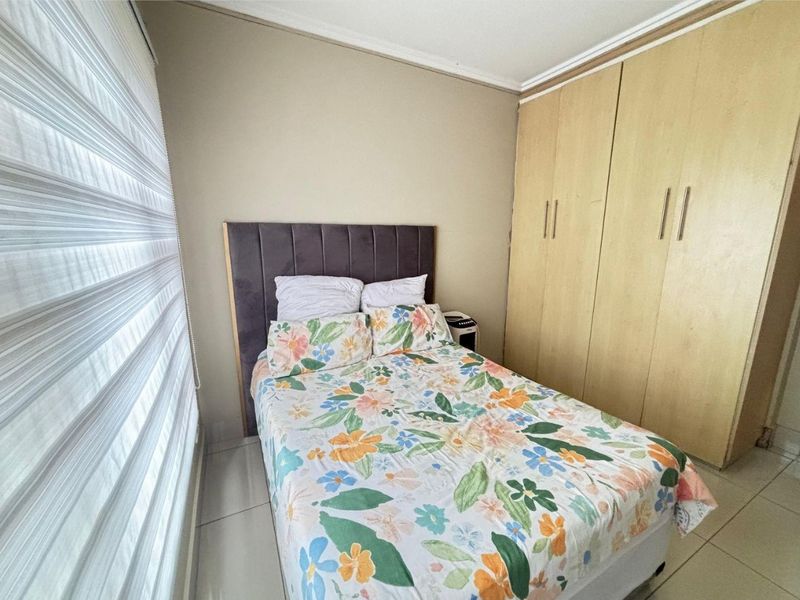 A functional bedroom featuring built-in wooden cupboards, tiled flooring, and modern roller blinds, providing a clean and practical living space.