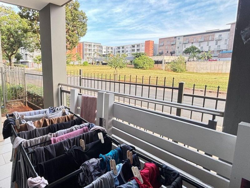 A covered balcony area featuring tiled flooring and a metal balustrade, offering an open view of the surrounding residential complex.