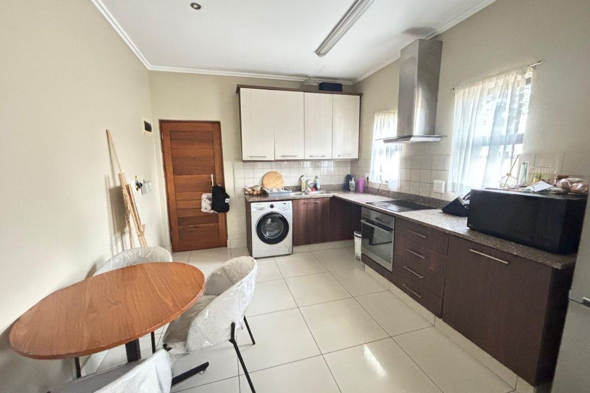Functional kitchen featuring two-tone cabinetry, granite countertops, built-in oven, hob, extractor fan, and integrated laundry plumbing with tiled flooring.