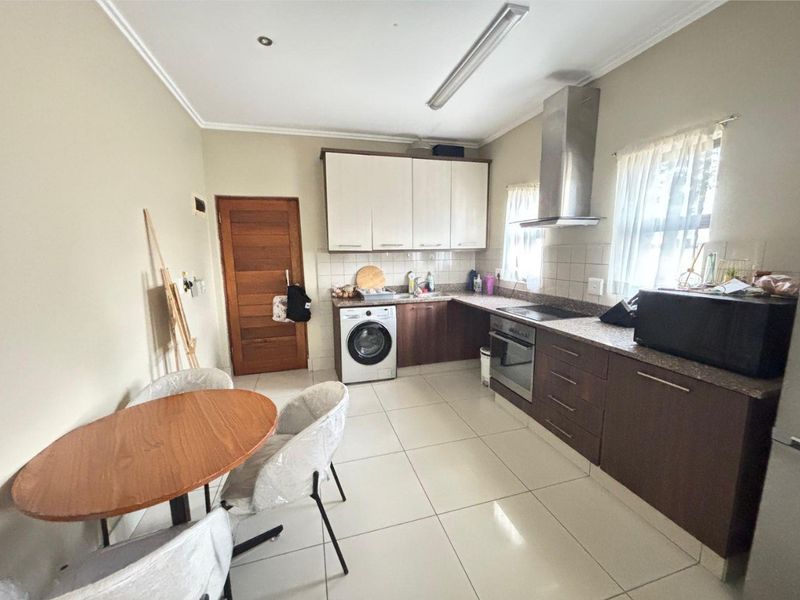 Functional kitchen featuring two-tone cabinetry, granite countertops, built-in oven, hob, extractor fan, and integrated laundry plumbing with tiled flooring.