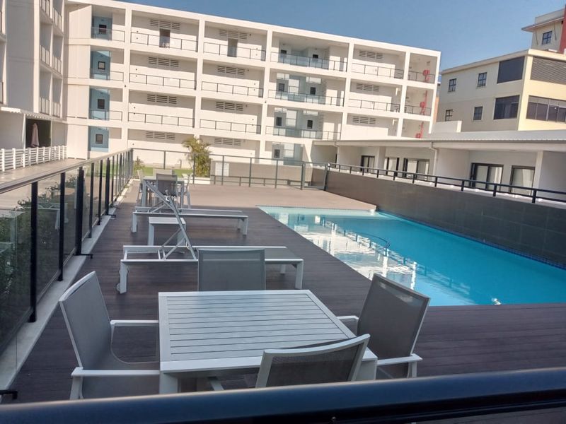 Communal swimming pool area featuring modern decking and glass balustrades, set within a well-maintained apartment complex.