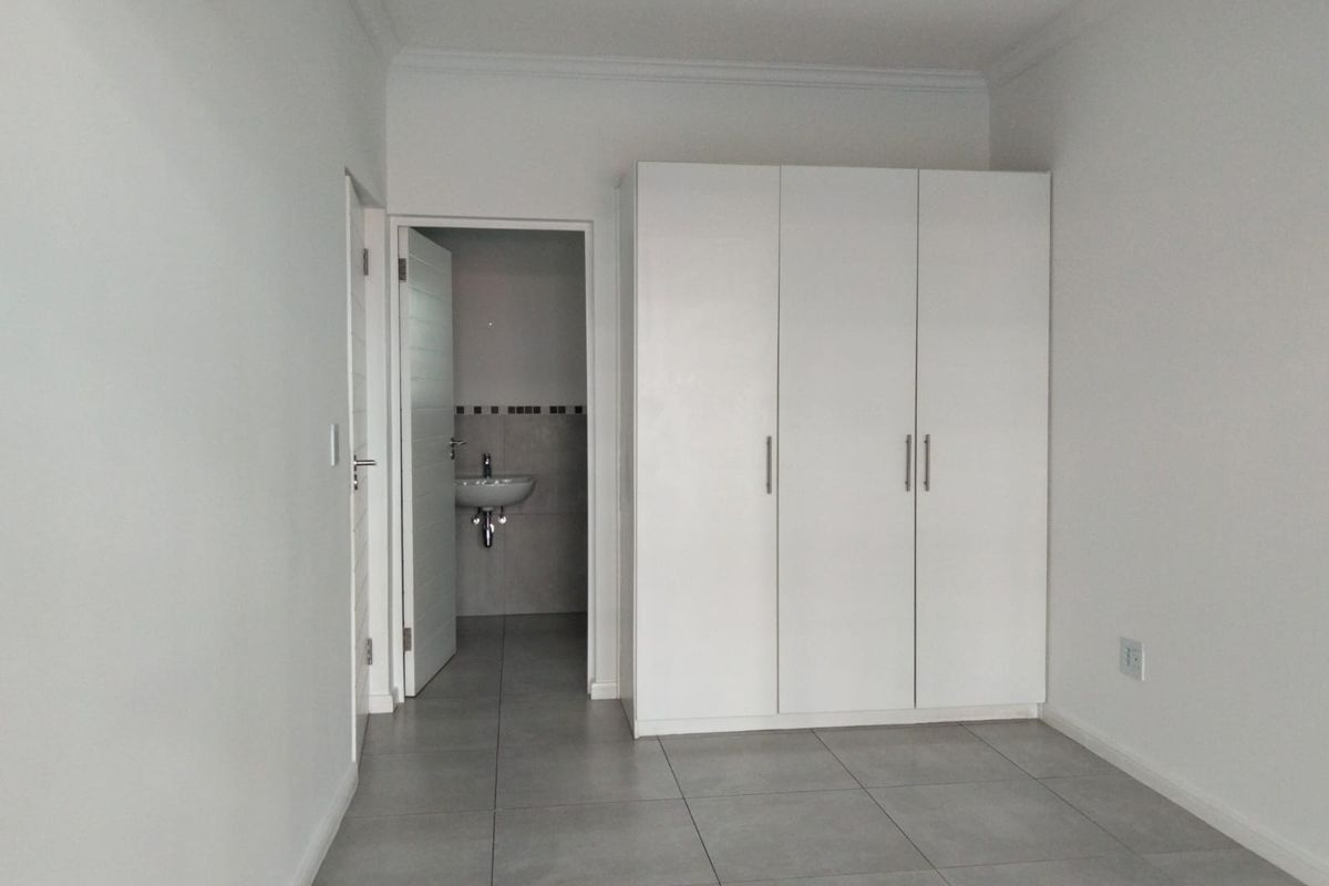 A clean, neutral bedroom featuring large-format floor tiles, a built-in wardrobe, and direct access to an en-suite bathroom.