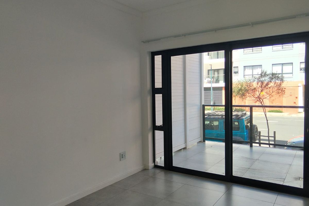 An empty living area featuring modern tiled flooring and a large sliding glass door providing access to an outdoor balcony.