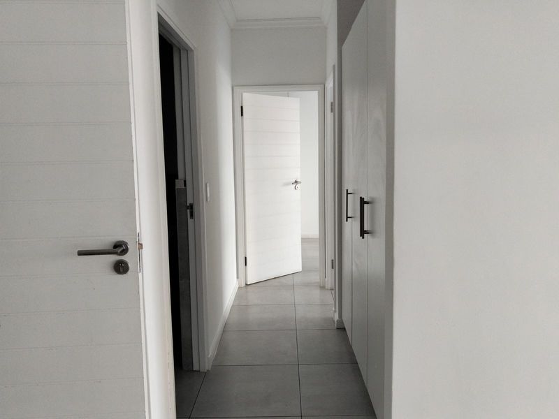 A clean, minimalist hallway featuring neutral tiled flooring, built-in storage cupboards, and modern internal doors leading to adjacent rooms.