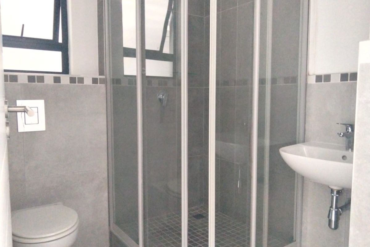A clean, modern bathroom featuring a glass shower enclosure, wall-mounted toilet, and a wall-hung basin with neutral grey tiling.
