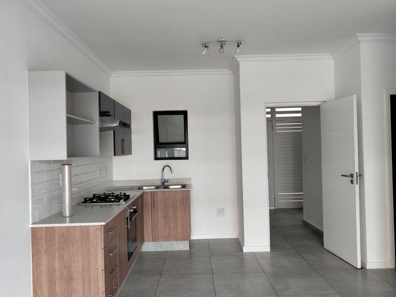 Modern kitchen featuring wood-finish cabinetry, stone countertops, gas hob, under-counter oven, and subway tile backsplash, with neutral tiled flooring throughout.