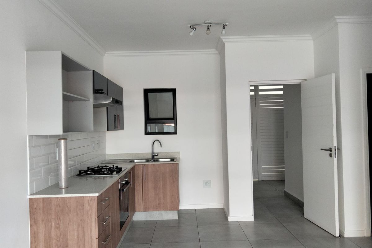 Modern kitchen featuring wood-finish cabinetry, stone countertops, gas hob, under-counter oven, and subway tile backsplash, with neutral tiled flooring throughout.