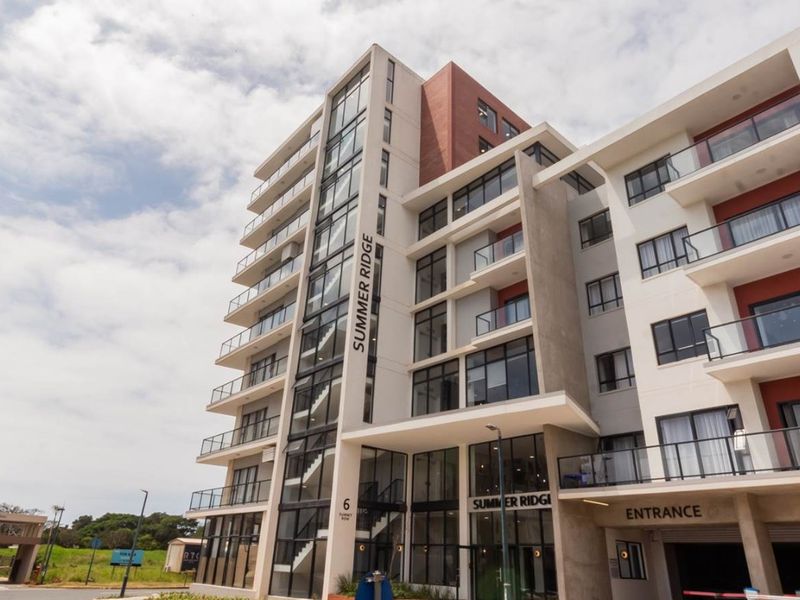 Modern multi-story apartment building facade featuring glass balconies, contemporary architectural design, and a dedicated vehicle entrance.