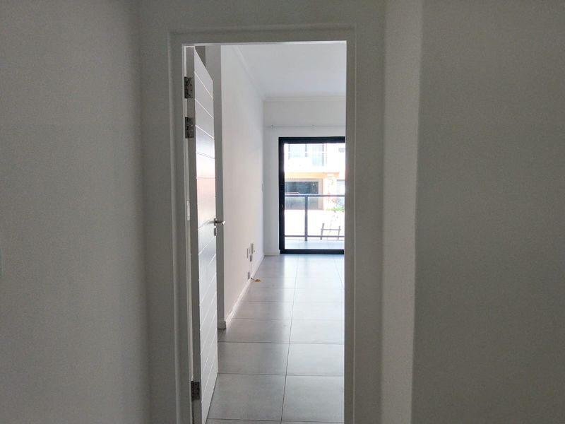 A bright, empty hallway with tiled flooring leading towards a sliding glass door that opens onto a balcony.