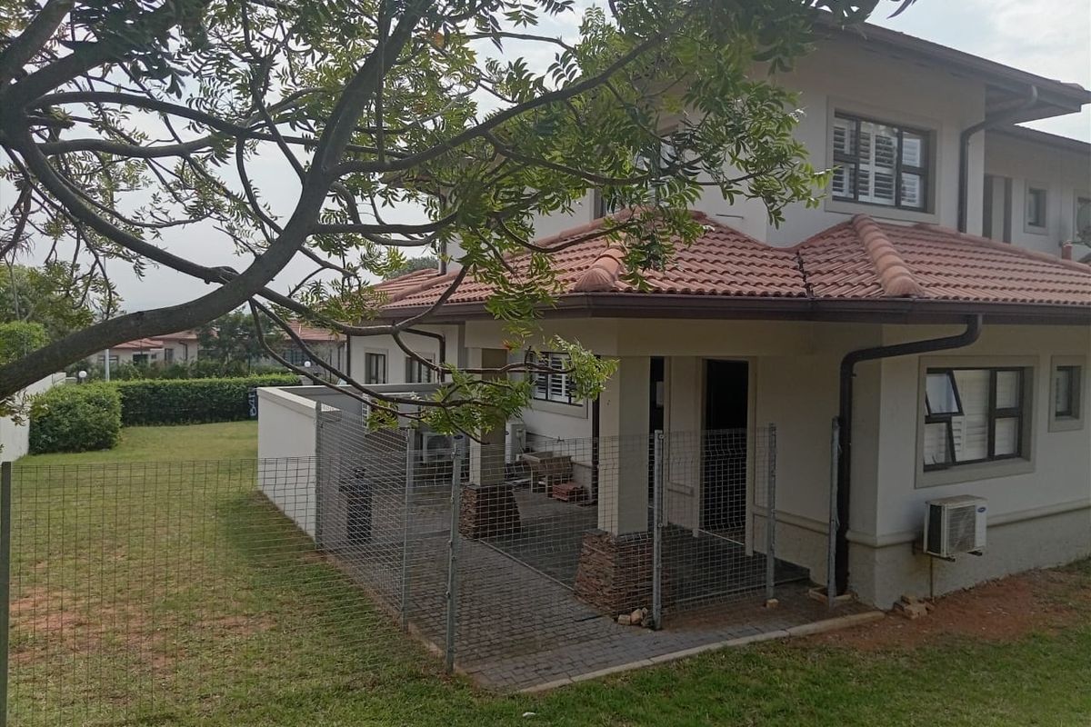 Rear view of the property featuring a covered patio with stone-clad pillars, paved flooring, and a surrounding garden area with wire mesh fencing.