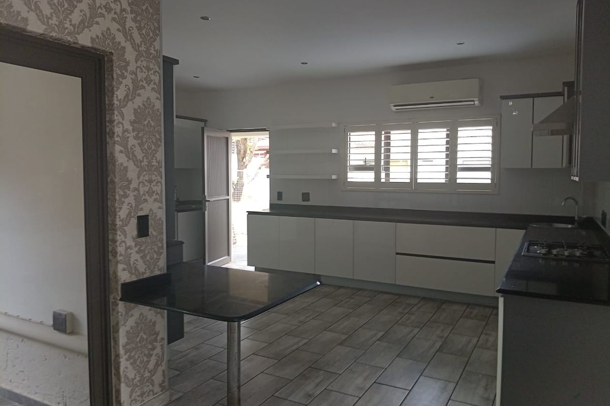 Modern kitchen featuring sleek white cabinetry, dark stone countertops, a gas hob, and tiled flooring with an integrated breakfast bar.