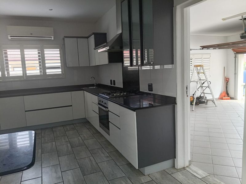 Modern kitchen featuring sleek two-tone cabinetry, granite countertops, integrated gas hob, oven, and extractor fan, complemented by tiled flooring and air conditioning.