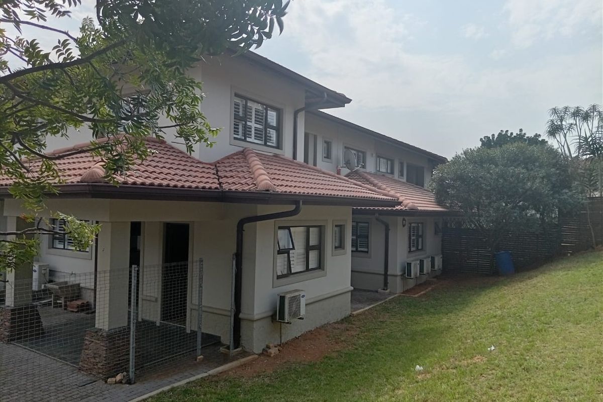 Rear view of a two-story residential property featuring a terracotta tiled roof, paved patio area, and established garden space.