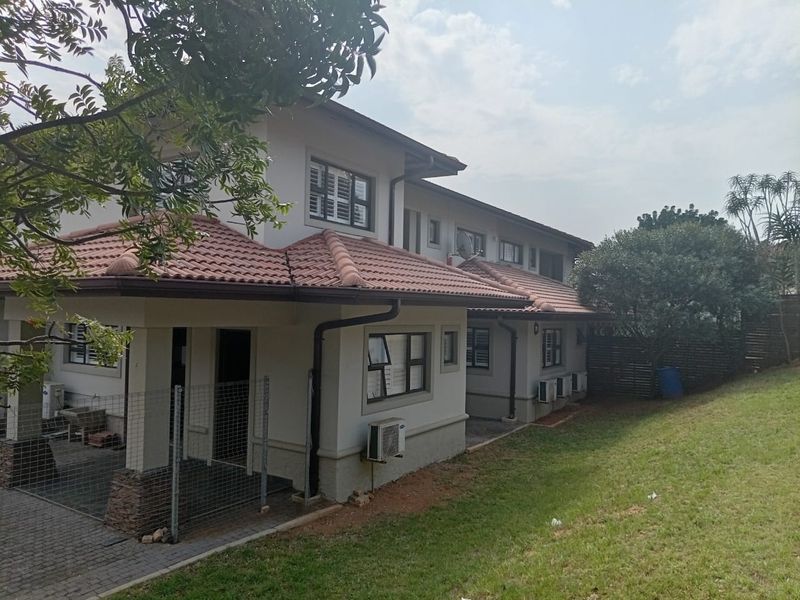 Rear view of a two-story residential property featuring a terracotta tiled roof, paved patio area, and established garden space.