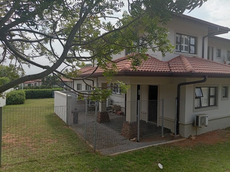 Rear view of the property featuring a covered patio with stone-clad pillars, paved flooring, and a surrounding garden area with wire mesh fencing.