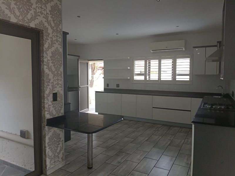 Modern kitchen featuring sleek white cabinetry, dark stone countertops, a gas hob, and tiled flooring with an integrated breakfast bar.