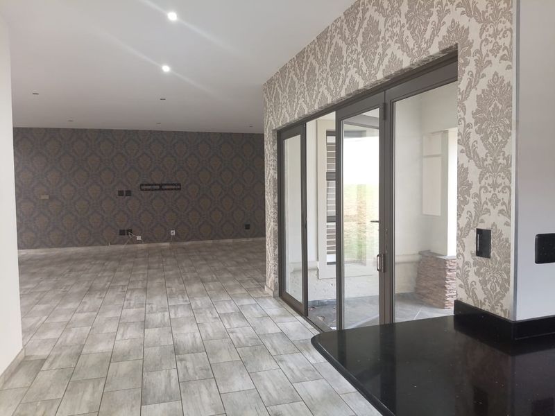 Spacious open-plan living area featuring modern tiled flooring, recessed lighting, and large aluminium sliding doors leading to an outdoor space.