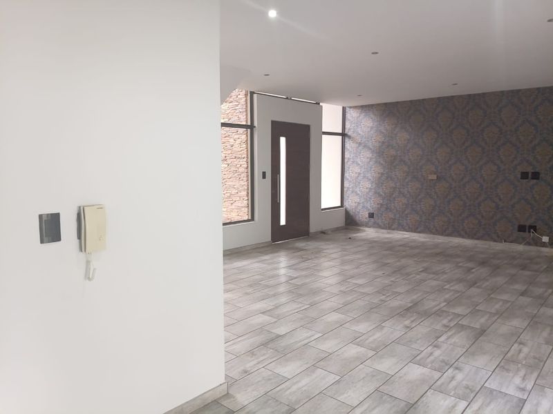 Spacious, empty living area featuring modern tiled flooring, recessed lighting, a feature wallpaper wall, and an intercom system near the entrance.