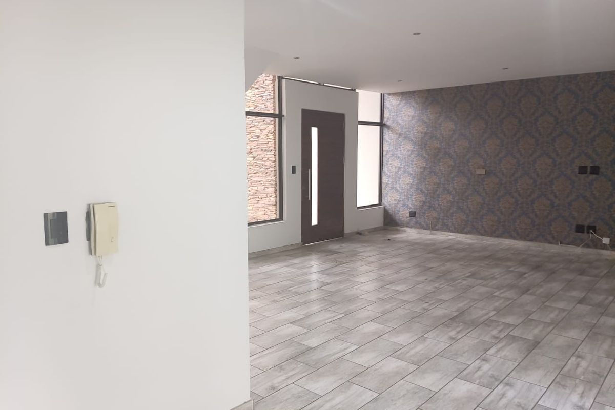 Spacious, empty living area featuring modern tiled flooring, recessed lighting, a feature wallpaper wall, and an intercom system near the entrance.