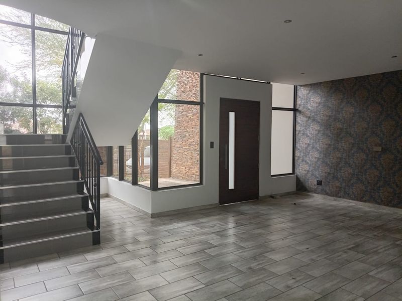 Spacious modern entrance hall featuring a striking staircase, large floor-to-ceiling windows, tiled flooring, and a decorative feature wall.