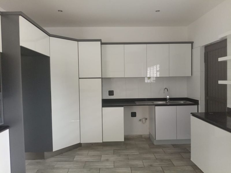 Modern kitchen featuring white high-gloss cabinetry, dark stone countertops, stainless steel sink, and neutral tiled flooring in a clean, contemporary layout.