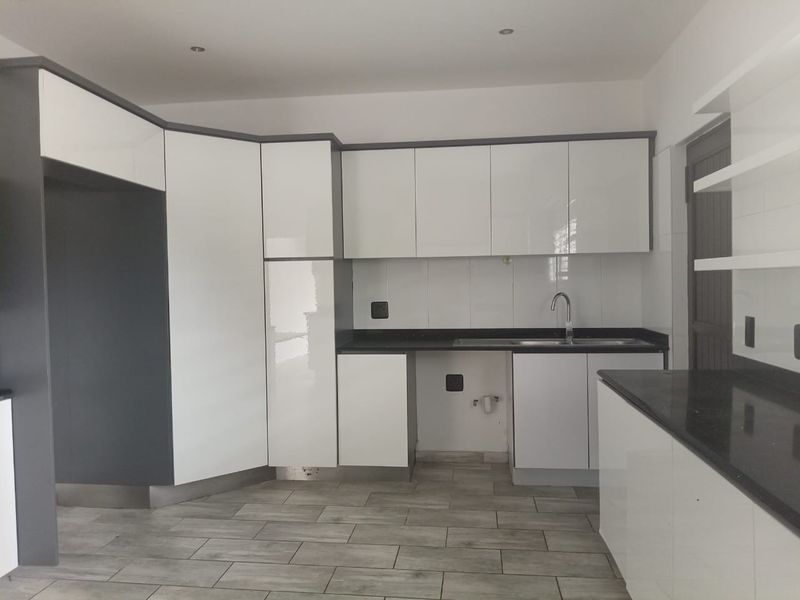 Modern kitchen featuring high-gloss white cabinetry, dark stone countertops, stainless steel sink, and contemporary tiled flooring in an open, clean space.
