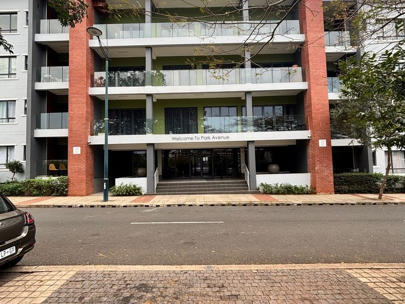 Front elevation of Park Avenue apartment complex featuring a modern brick facade, glass balconies, and a paved entrance area.