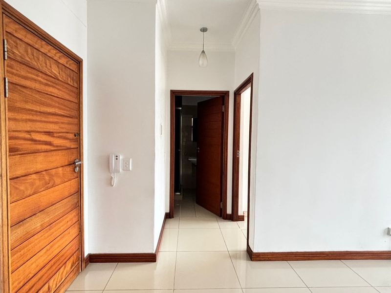 A clean, well-maintained hallway featuring neutral tiled flooring, classic wooden doors, and decorative cornicing, providing access to multiple rooms.