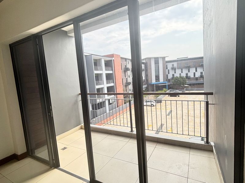 A clean, modern balcony featuring large format floor tiles, a metal safety railing, and expansive sliding glass doors providing access to the apartment.